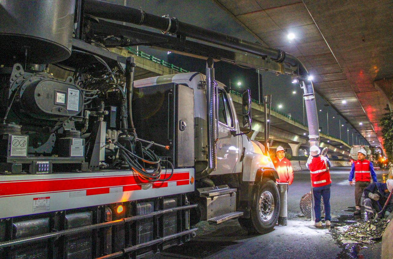Des ouvriers nettoient les rues avec des machines sous un viaduc, de nuit.